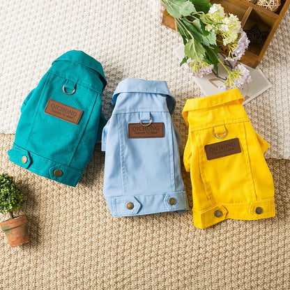 Gros plan sur trois vestes en denim pour chien Billie de couleurs turquoise, bleu ciel et jaune, présentées avec des fleurs de cerisier et un panier en bois sur un tapis tressé.