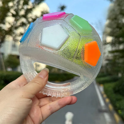 Balle de jeu transparente pour chien en forme de ballon de football américain, dotée d'une poignée centrale intégrée et de facettes colorées (rose, vert, orange, blanc). Une main tient le jouet en extérieur.