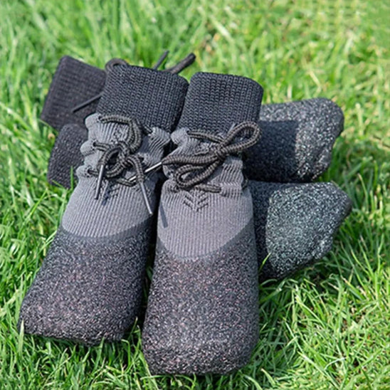 Paire de chaussures Paw Control pour chien posée sur l'herbe, montrant le design montant en tricot noir et les semelles de protection robustes pour l'extérieur.