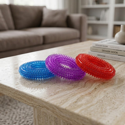 Trois anneaux de dentition pour chien Hop-Là aux couleurs vives (bleu, violet, rouge) posés sur une table basse de salon.