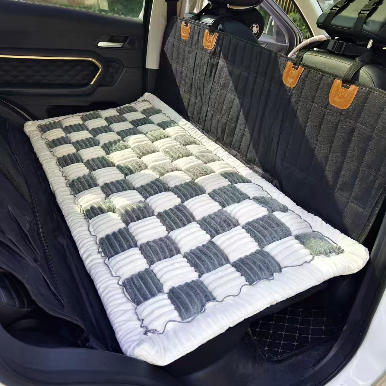 Vue intérieure d'une voiture montrant une housse de protection noire matelassée sur la banquette, recouverte d'un tapis moelleux à damier gris et blanc.