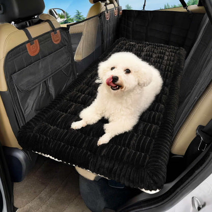 Petit chien blanc assis confortablement sur une housse de protection matelassée noire installée sur la banquette arrière d'une voiture.