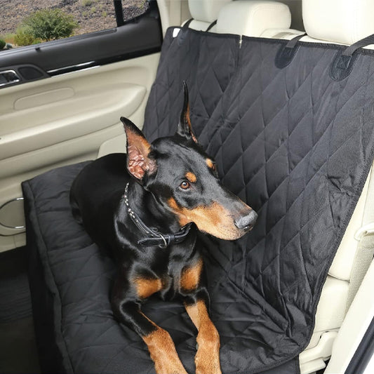 Chien Dobermann noir et feu assis sur la housse de voiture CozyCar noire au motif matelassé, illustrant la protection complète de la banquette arrière et le confort du matériau en polyester.