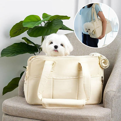 Petit chien blanc de type Bichon confortablement installé dans un sac de transport en coton beige posé sur un fauteuil, à côté d'une plante verte.