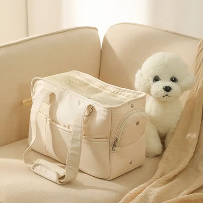 Petit chien blanc de type Bichon assis sur un canapé à côté du sac de transport en coton beige, dont la fermeture éclair latérale est entrouverte.