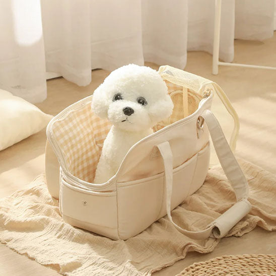 Petit chien blanc de type Bichon assis à l'intérieur d'un sac de transport en coton beige ouvert, révélant une doublure à motif vichy jaune et blanc.