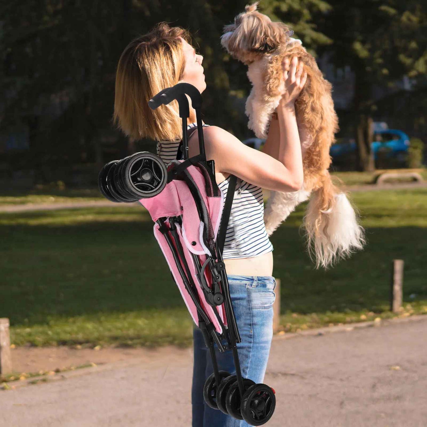 Femme portant la poussette pour chien rose Passe-Partout pliée sur l'épaule tout en tenant son petit chien, illustrant la légèreté et la facilité de transport.