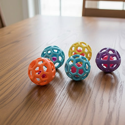 Quatre balles interactives en caoutchouc ajouré de différentes couleurs posées sur une table en bois pour le jouet Pitou bounce.