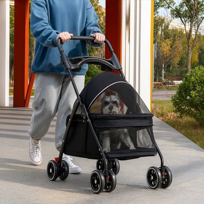 Poussette pour chien MobilConfort noire avec un Schnauzer à l'intérieur, tenue par une personne en promenade dans un parc, montrant les fenêtres en mesh respirant.