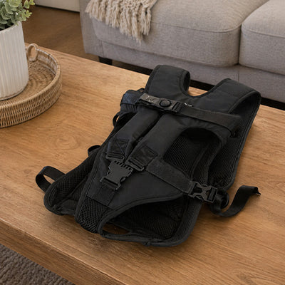 Sac de transport pour chien noir en tissu mesh respirant posé sur une table, montrant les boucles de sécurité et la structure ergonomique du harnais.