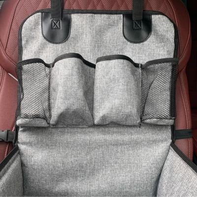 Zoom sur les trois compartiments de rangement en filet du siège auto Sécuri-Voyage, montrant la texture du tissu gris chiné et l'installation sur un siège de voiture rouge.